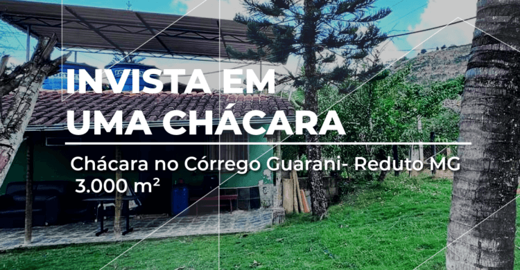 Foto de uma chácara com gramado verde, casa com telhado colonial, árvores e céu azul, localizada no Córrego Guarani, Reduto MG. Imagem promocional da imobiliária Manassés Soluções Imobiliárias com o texto “Invista em uma chácara”.