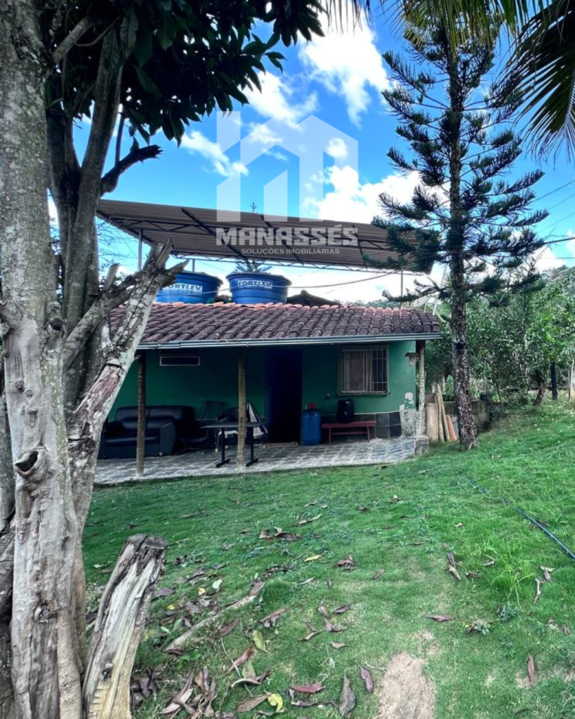 Fachada de casa simples com telhado colonial e varanda, cercada por árvores e gramado verde, em chácara localizada no Córrego Guarani, Reduto MG.