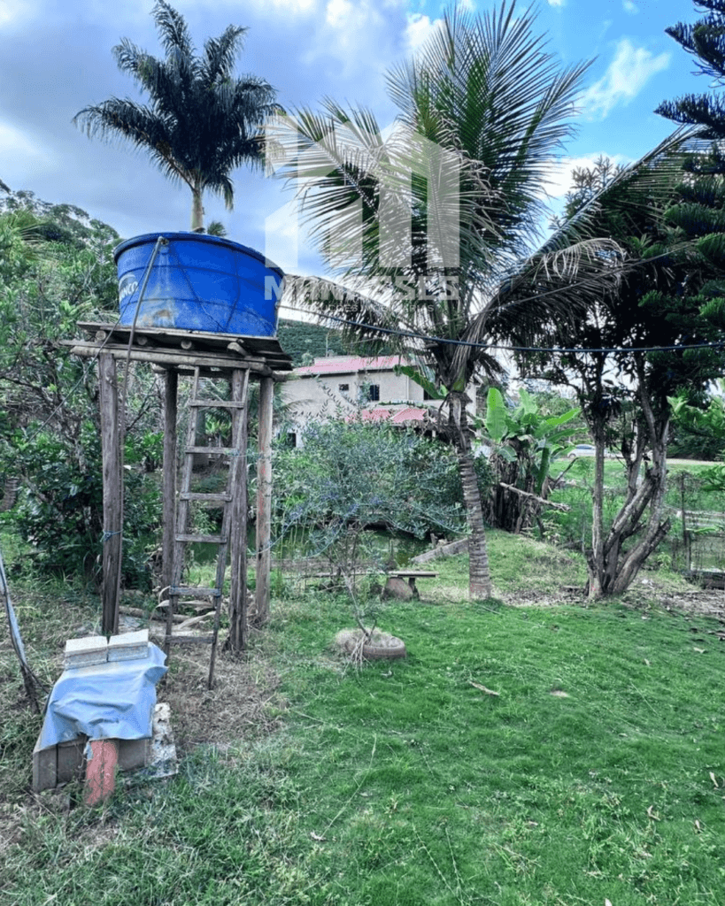 Caixa d’água azul elevada sobre estrutura de madeira em área gramada com árvores e vegetação, localizada em chácara no Córrego Guarani, Reduto MG.