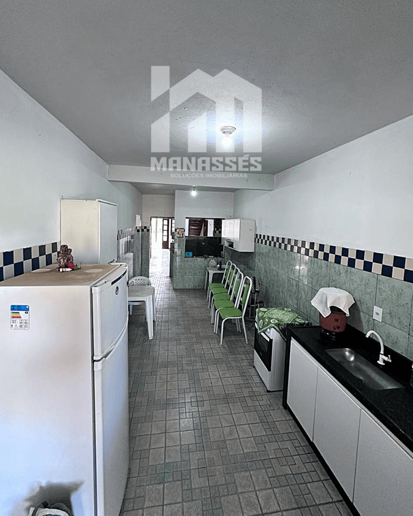 Cozinha comprida com azulejos verdes e detalhes em azul, equipada com armários e eletrodomésticos – Manassés Soluções Imobiliárias.