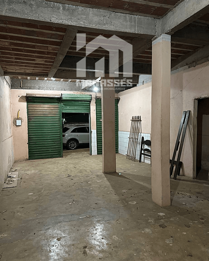 Área interna com colunas, piso cimentado e portas de aço verdes – Manassés Soluções Imobiliárias.