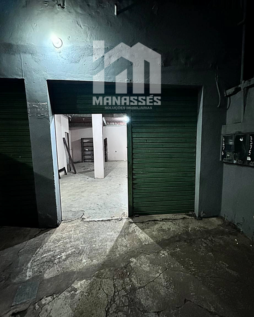 Entrada com porta de aço verde parcialmente aberta para espaço interno – Manassés Soluções Imobiliárias.