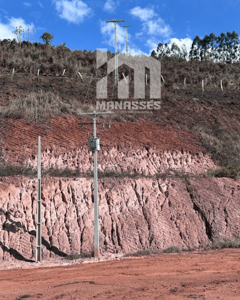 Terreno com poste elétrico e transformador instalado, solo avermelhado e declive natural em Manhuaçu/MG, ideal para empreendimentos industriais ou comerciais.