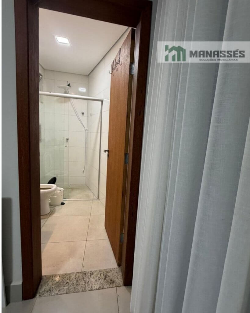 Acesso ao banheiro da suíte com revestimento cerâmico, box em vidro temperado e acabamento moderno em imóvel residencial à venda em Manhuaçu.