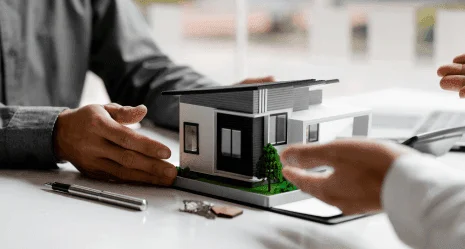Duas pessoas em torno de uma mesa observando e apontando para uma maquete de casa moderna em miniatura.