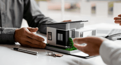Duas pessoas em torno de uma mesa observando e apontando para uma maquete de casa moderna em miniatura.