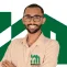 Pessoa sorridente usando camisa bege com logo verde da Manassés Soluções Imobiliárias sobre fundo branco.