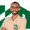 Pessoa sorridente usando camisa bege com logo verde da Manassés Soluções Imobiliárias sobre fundo branco.
