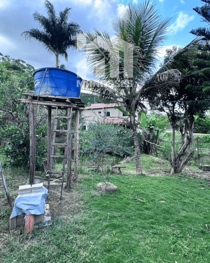 Caixa d’água azul elevada sobre estrutura de madeira em área gramada com árvores e vegetação, localizada em chácara no Córrego Guarani, Reduto MG.